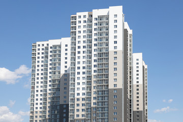 Fototapeta na wymiar High white-grey multi-family dwelling building against blue sky