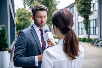 journalist holding microphone and talking with businessman in formal wear