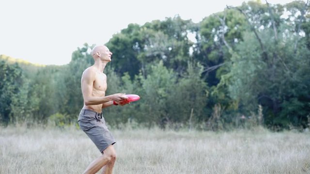 Slow Motion Of young slim athletic man with bare torso catching and throwing frisbee. Active several friends Playing Frisbee in park. Group of active friends spending time together outdoors.