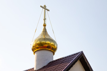 Close-up of gilded christian church dome with cross on top on red roof against white sky