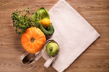 Fresh vegetables, pumpkins, cabbage leaf with green grass in pot, flatlay on eco bag and wooden background table