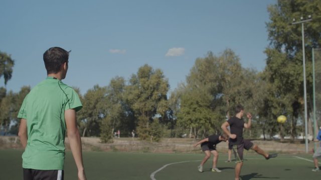 Rear view of young street soccer player taking throw-in and passing ball to teammates during football game on pitch. Offensive team returning to attack opponent goal after throw-in during soccer match