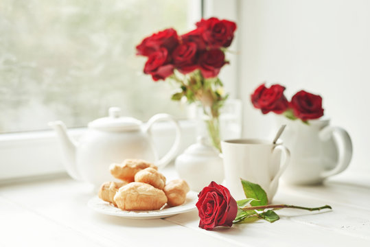 red roses, tea and croissants on a table near the window, romantic breakfast for Valentine's Day