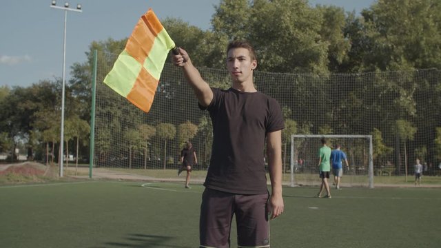 Portrait of concentrated soccer assistant referee moving along touchline and signalling offside offence trap during football match. Linesman signals for offside by raising his flag during soccer game.