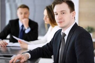 Businessman headshot at meeting in modern office. Unknown entrepreneur sitting with colleagues at the background. Teamwork and partnership concept