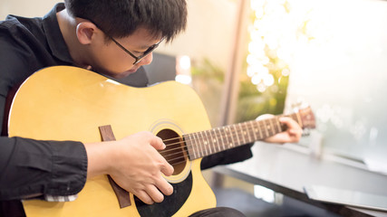 Young Asian man guitarist playing music with classic guitar at home. String musical instrument for recreational activity or personal hobby. Relaxation and entertainment concepts