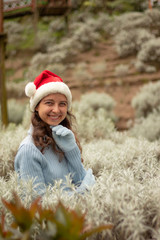 Portrait of young woman wearing red santa hat and blue gloves. Pretty Caucasian woman smiling and touching her chin. Christmas and New Year celebration.