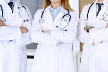 Group of modern doctors standing as a team with arms crossed in hospital office, close-up. Physicians ready to examine and help patients. Medical help, insurance in health care, best treatment and