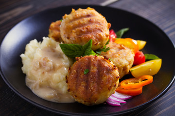 Fish cakes with mashed potatoes and vegetables, garnished with basil. Fish burgers on black table. Horizontal image