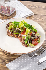 Spicy roastbeef Salad with green mix and tomato on white plate on wooden table