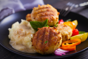 Fish cakes with mashed potatoes and vegetables, garnished with basil. Fish burgers on black table. Horizontal image