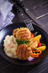 Fish cakes with mashed potatoes and vegetables, garnished with basil. Fish burgers on black table. Vertical image