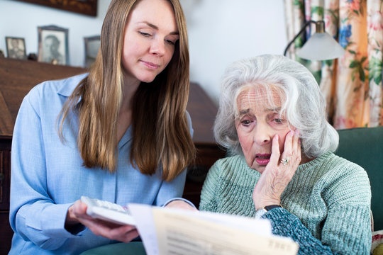 Woman Helping Worried Senior Neighbor Concerned About Debt With Bills And Paperwork