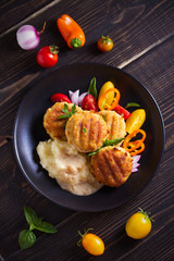 Fish cakes with mashed potatoes and vegetables, garnished with basil. Fish burgers on black table. Overhead, vertical image