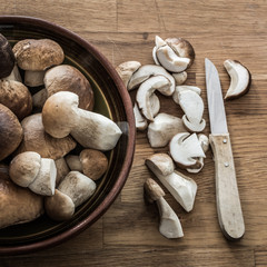 Whole and sliced porcini in a bowl on wooden table - square, high angle view