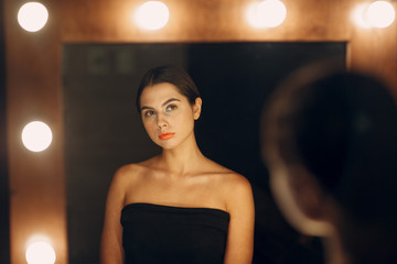 Beautiful young woman doing makeup near the mirror with lamps