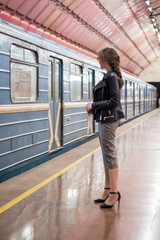 Business woman with a cup of coffee at subway station and train. Beautiful girl in sunglasses and a jacket at the subway station. Fashionable and stylish girl. Success concept