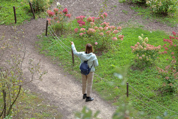 Unknown caucasian girl in checkered pants stands in a flowering meadow in the park
