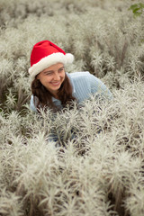 Portrait of young woman wearing red santa hat and blue gloves. Happy Christmas and New Year celebration. Pretty Caucasian woman with charming smile in edelweiss valley.