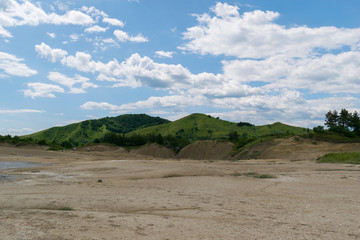 contrast between arid soil in the foreground and green hills in the background with beautiful blue sky