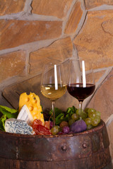 Red and white wine with  grapes on old cask in wine cellar. Glasses and bottles of wine with cheese, jamon, figs and nuts