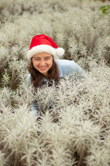 Portrait of young woman wearing red santa hat and blue gloves. Happy Christmas and New Year celebration. Pretty Caucasian woman with charming smile in edelweiss valley.