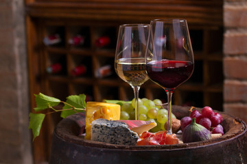 Red and white wine with  grapes on old cask in wine cellar. Glasses and bottles of wine with...