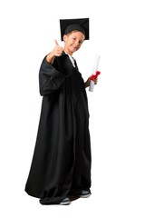 Full body of Little boy graduating giving a thumbs up gesture and smiling on isolated white background
