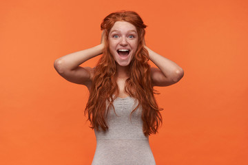 Studio shot of lovely overjoyed young female with wavy foxy lond hair posing over orange...
