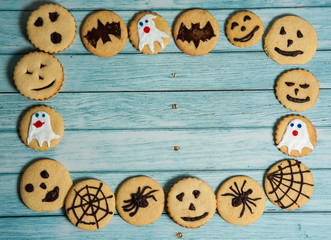 Fototapeta premium The Concept Of Halloween. The frame is made of terribly delicious homemade cookies with bats, spiders, ghosts, horrible emojis, cobwebs on a light blue wooden background.