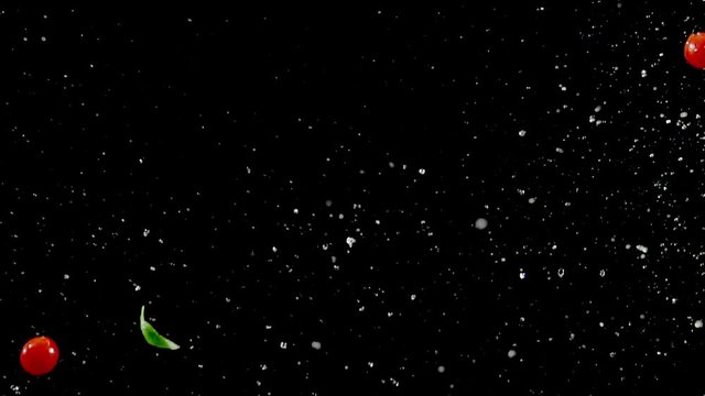 Cherry tomatoes and basil with water droplets collide on black background closeup in super slow motion