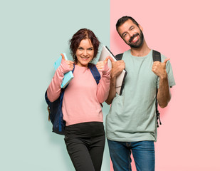 Two students with backpacks and books giving a thumbs up gesture and smiling because has had success on colorful wall