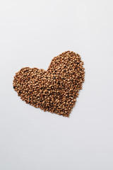 Raw buckwheat on white background shaped as heart symbol and tape measure