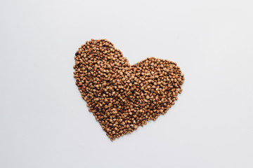 Raw buckwheat on white background shaped as heart symbol and tape measure