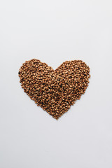 Raw buckwheat on white background shaped as heart symbol and tape measure