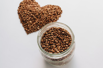 Raw buckwheat on white background shaped as heart symbol and tape measure