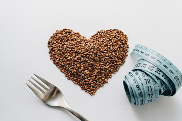 Raw buckwheat on white background shaped as heart symbol and tape measure