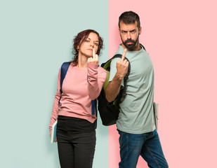 Two students with backpacks and books making horn gesture. Negative expression on colorful wall