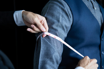 The dressmaker was using a tape measure to measure the length of the arm on a black background.