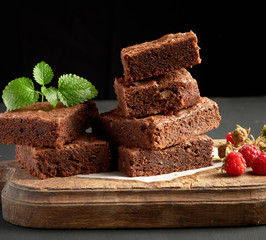 stack of baked square pieces of chocolate brownie cake on brown wooden cutting board