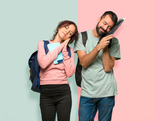 Fototapeta premium Two students with backpacks and books making sleep gesture. Adorable sweet expression on colorful wall