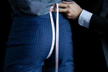 The dressmaker used a tape measure to measure the length of the butt on a black background.