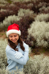 Portrait of joyful pretty woman wearing red santa hat and blue gloves. Young Caucasian woman with charming smile. Christmas and New Year holidays.