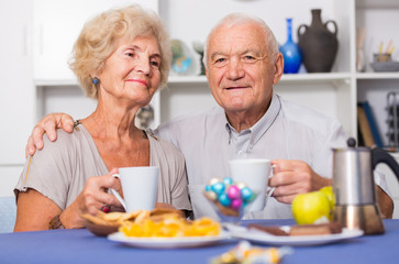 Fototapeta na wymiar Smiling elderly spouses enjoying tea with sweets