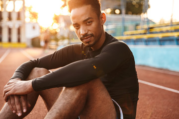 Image of african american man sitting at sports ground outdoors
