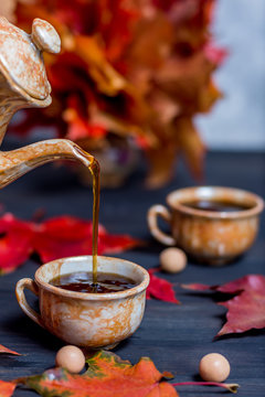 Morning coffee in mugs and a coffee pot pours coffee in a mug on a dark wooden background with maple leaves