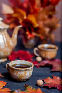 Morning coffee in mugs and coffee pot on a dark wooden background with maple leaves