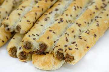 Sticks with meat from puff pastry, sprinkled with flax seeds. Freshly baked puffed straws with meat on a white table. Delicious homemade baked goods with stuffing.