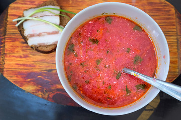A plate with a red borscht on a wooden board close-up. Lunch menu borscht with sour cream and rye bread with bacon and green onions. Delicious nourishing homemade food top view.