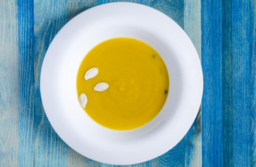 pumpkin soup in white plate on blue wooden background